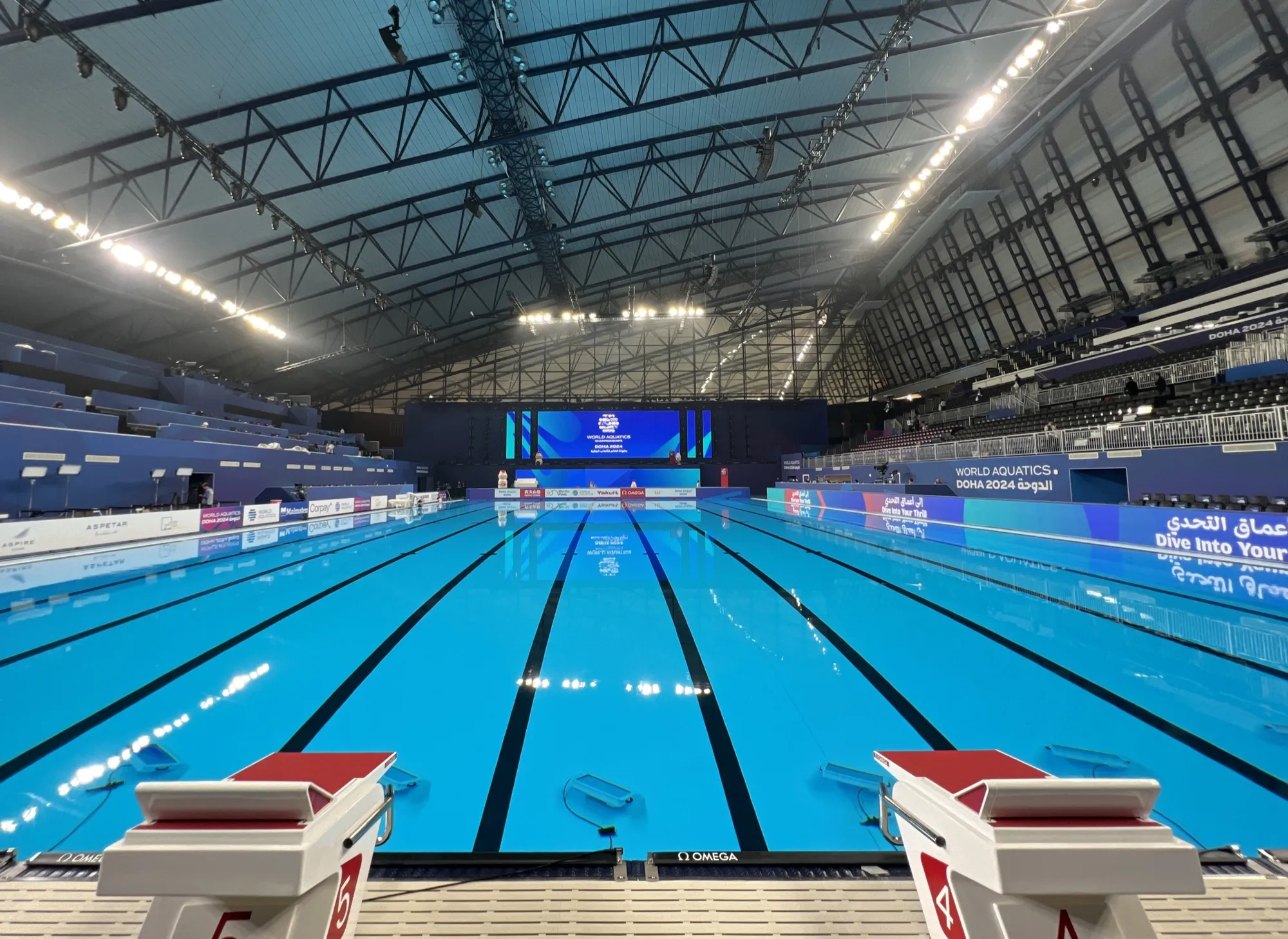 Olympic swimming pool beneath long-span steel roof trusses at Aspire Dome, Doha