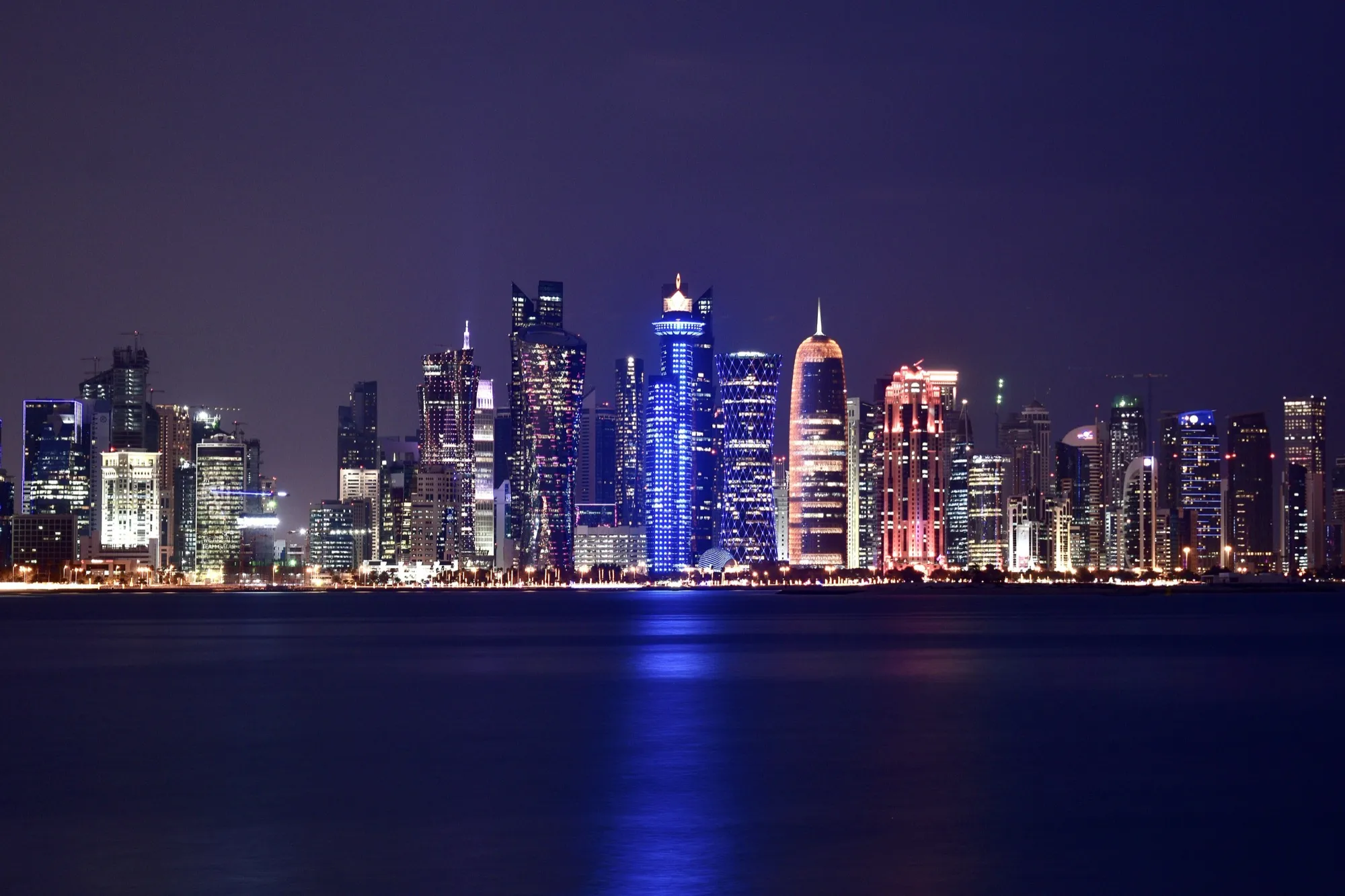Illuminated glass towers of the West Bay skyline at night across the water, Doha